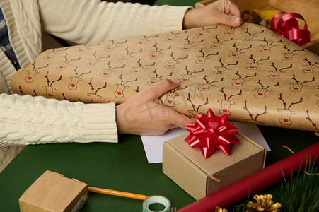 在包装圣诞礼物时，女人的手的特写镜头推出带有鹿图案的包装纸。