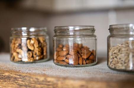 向日葵种子、核桃和杏仁放在一个罐子里，罐子放在一张白色的老式桌子上，背景是厨房。