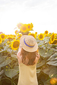 一大片向日葵花田上，一个身穿黄色连衣裙、头戴草帽的女孩背着手捧着一束向日葵。