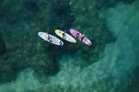 蓝色水摄影照片_在美丽的蓝色水面上，在 SUP 立式桨板上的瑜伽正上方的空中无人机视图