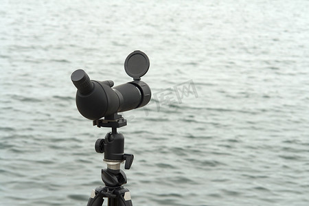 镜头变焦摄影照片_水边三脚架上的单筒观鸟观察镜