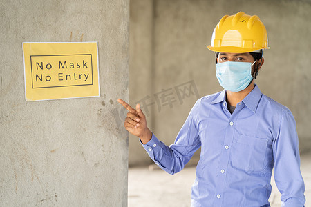 工人在工作建筑工地的墙上指着“禁止面罩禁止进入”标牌布告牌，以防止在工作场所受到冠状病毒或 covid-19 的侵害-大流行期间的健康和劳动安全概念