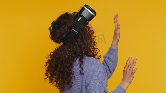 游戏应用摄影照片_使用虚拟现实耳机头盔玩模拟游戏应用、观看视频内容的年轻女性