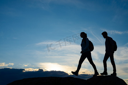 运动徒步蓝色摄影照片_年轻快乐的旅行者在夏日日落时背着背包在岩石小径上徒步旅行。