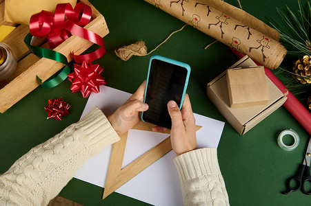 有选择地关注女性手拿着带有复制广告空间的智能手机，背景是圣诞包装材料