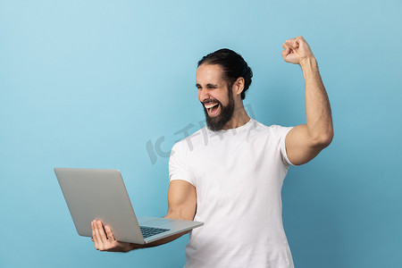男人高兴地尖叫着拿着笔记本电脑，为胜利而欢欣鼓舞，在线投注。