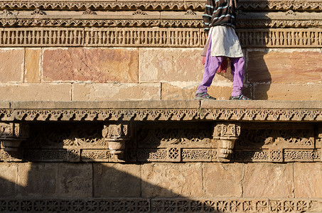 走在雕刻在 Adalaj Stepwell 石墙上的美丽边界图案和设计上的印度妇女