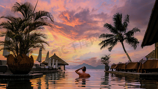 豪华游泳池热带度假村，假期塞舌尔群岛，日落时分在游泳池旁的年轻人