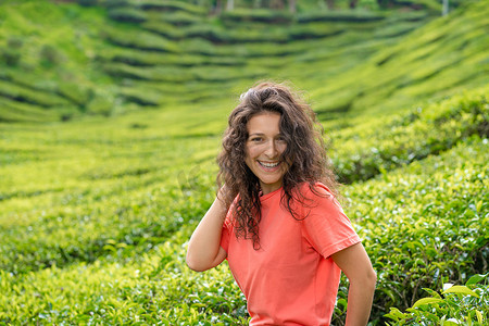 茶谷摄影照片_美丽的黑发女孩摆在绿茶灌木丛之间的茶谷中间。