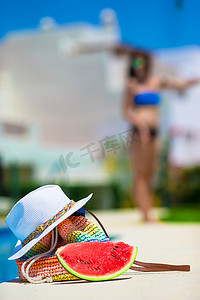 夏日概念 — 美味的西瓜、草袋和果汁，靠近泳池户外背景的年轻女性
