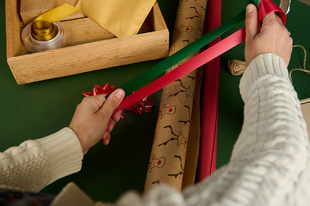 从上方看女人的手拿着红绿缎面装饰带，在艺术车间包裹礼品纸