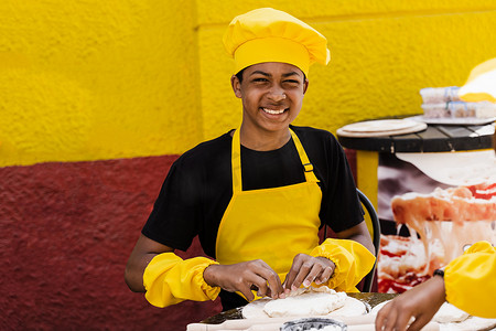 身着厨师帽和黄色围裙制服的非洲黑人少年在面包店做饭。