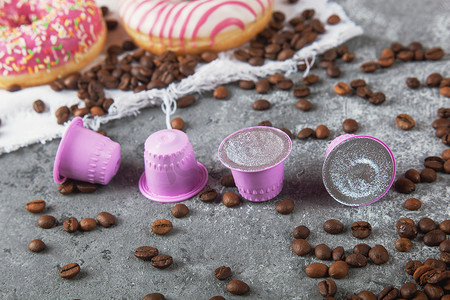 塑料箔纸摄影照片_浓咖啡粉色塑料胶囊，配有箔纸、咖啡豆和甜甜甜圈