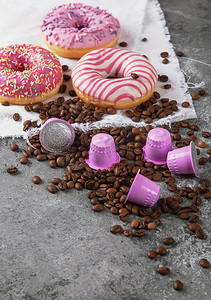 塑料箔纸摄影照片_浓咖啡粉色塑料胶囊，配有箔纸、咖啡豆和甜甜甜圈