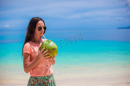 天气炎热摄影照片_在阳光明媚的炎热天气里，年轻漂亮的女人手里拿着一个大椰子