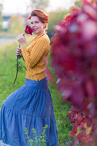 美丽的女人在红色野藤叶丛附近拿着玫瑰的画像