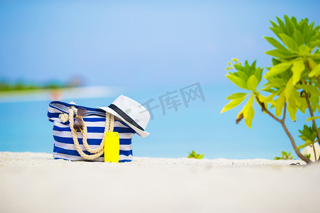 白色沙滩上的蓝色包、草帽、太阳镜和防晒瓶