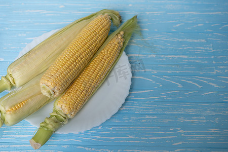 绿叶玉米芯位于白盘蓝色背景上。