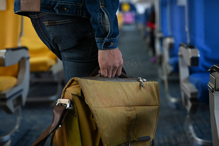 男乘客提着包在飞机过道上行走的形象。