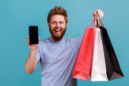 男人满意地站着，展示购物袋和黑屏智能手机。