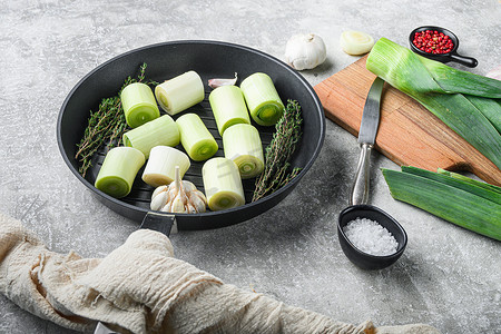生炖韭菜苏丹在烤盘上未煮熟的香草成分，灰色纹理背景侧视图。