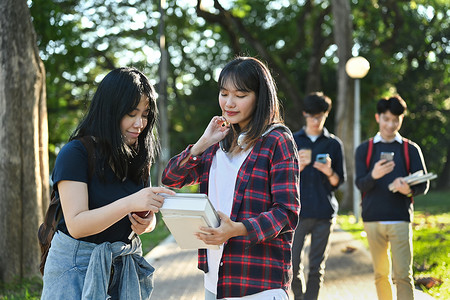 两名友好的女学生在大学校园户外散步时在课后互相交谈的照片