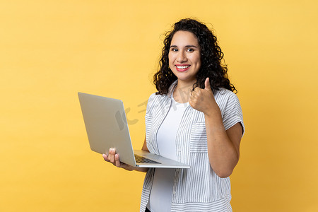 友好快乐开朗的女人在笔记本电脑上工作，看着相机屏幕，竖起大拇指。