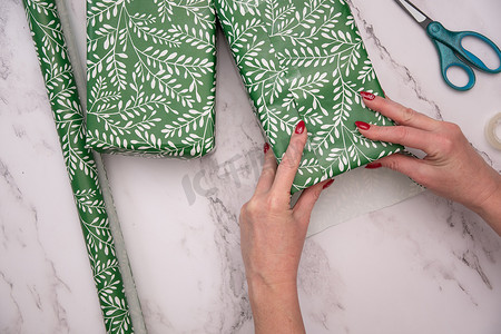 美甲贴纸新年摄影照片_女人手上涂着红色圣诞美甲，用绿色包装纸包裹礼物