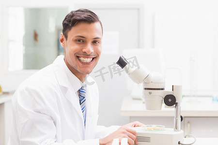 医学观察中摄影照片_微笑的科学家用显微镜观察培养皿