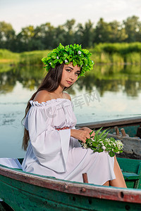 这位仙女留着长长的黑发，穿着一件白色的复古连衣裙，坐在河中央的一条船上。