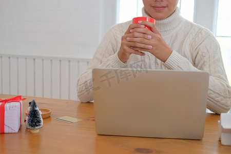 男人拿着咖啡杯 & 在圣诞节期间在家里使用电脑。