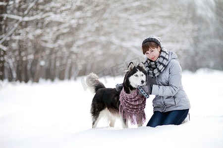 在冬天的森林里，女孩和一只西伯利亚哈士奇狗坐在雪地里