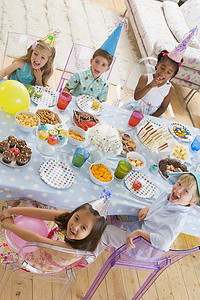 活动派对摄影照片_派对上的年幼孩子坐在桌边，面带微笑地吃着食物