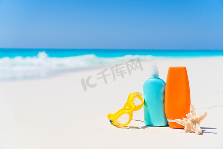 白色沙滩背景海洋上的防晒霜瓶、护目镜、海星
