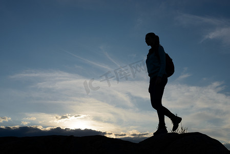 年轻女子旅行者在夏季日落时背着背包在美丽的岩石小径上徒步旅行。