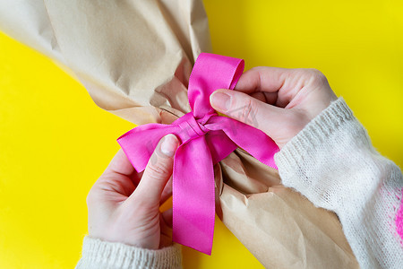 在黄色背景上用粉色丝带和礼物绑一束女性手的顶视图。