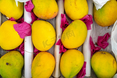 一张成熟的黄绿色芒果放在白纸上，上面覆盖着粉红色的黄油纸，准备出售和供应