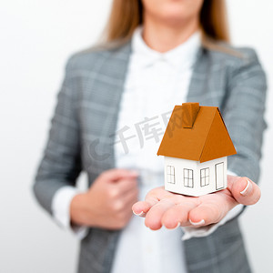 一只手拿着彩色纸房子的灰色西装的女商人。