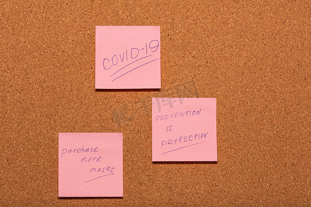 Covid-19，预防就是保护，并提醒购买更多面具，手写在软木告示板上的三张粉色贴纸上。