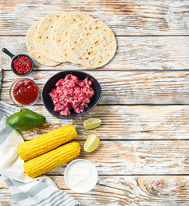 用黑色碗里的碎有机牛肉、玉米、卡尔萨在白色质感的木桌上烹制墨西哥炸玉米饼配料，顶视图有文字空间。
