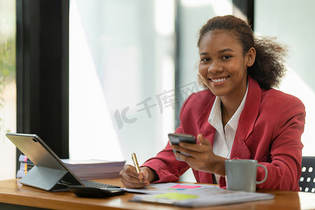 非裔美国女商人使用计算器和笔记本电脑在办公室和商业工作背景、税务、会计、统计和分析研究概念的木桌上进行数学金融