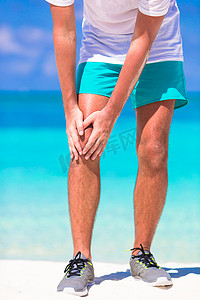 在白色沙滩上锻炼时腿部疼痛的男运动员