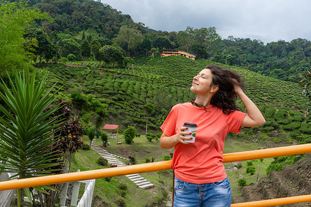 茶谷摄影照片_在绿茶谷的背景下，黑发旅游女孩享用工艺杯中的茶。