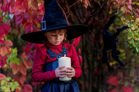万圣节的帽子摄影照片_打扮成女巫的小女孩在万圣节派对上拿着蜡烛。