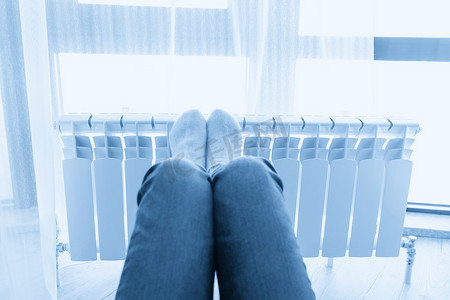 冷色调摄影照片_穿着羊毛袜、脚放在加热器上取暖的女人