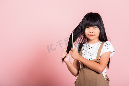 外国小孩子摄影照片_10 岁的亚洲小孩拿着梳子不守规矩地刷她，她摸着她长长的黑发
