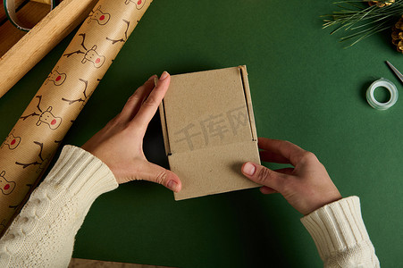 顶视图女人的手把圣诞礼物装在绿色表面的纸箱里，上面放着包装装饰纸