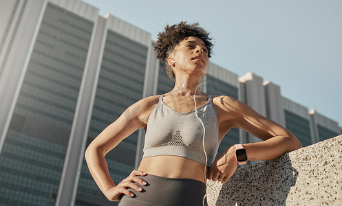 黑人女性、城市健身和音乐耳机，用于从下方在城市城镇进行体育运动、锻炼和锻炼。