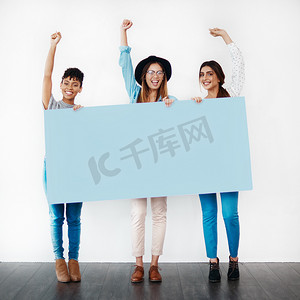 为你所相信的事情挺身而出。工作室拍摄的一群年轻女性拿着一张空白的标语牌，在白色背景下欢呼。
