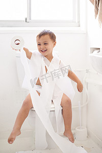 如厕训练摄影照片_如厕训练可能是一项挑战......一个小男孩坐在用卫生纸包裹的马桶上的幽默镜头。
